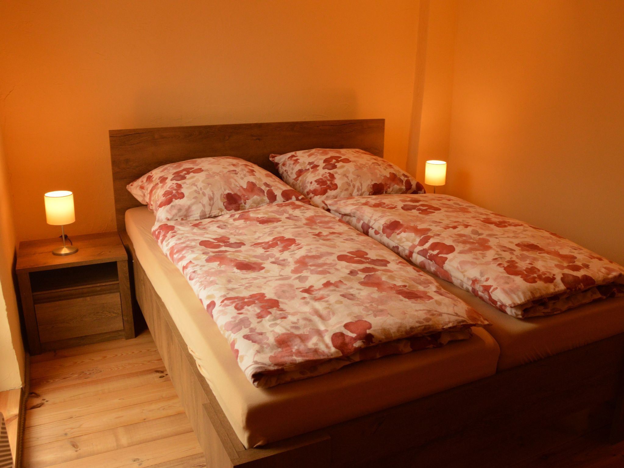 Un letto matrimoniale con biancheria da letto floreale, due lampade ai lati del letto e una testiera in legno.