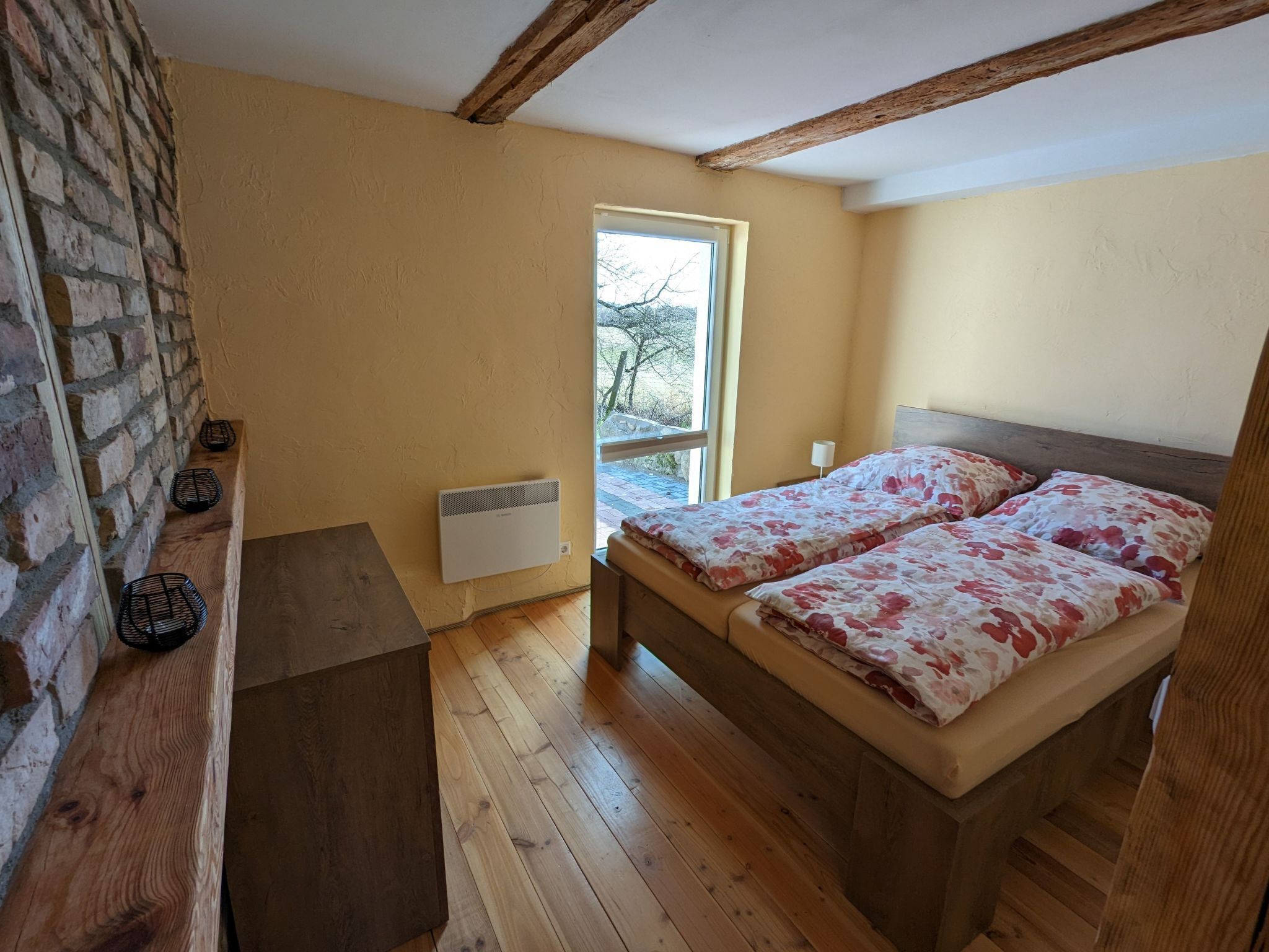 A bedroom with a wooden bed, a window, a radiator, and a brick wall.