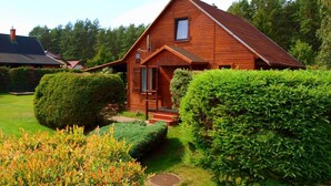 Una baita in legno con tetto spiovente, un portico e un giardino curato con arbusti e prato.