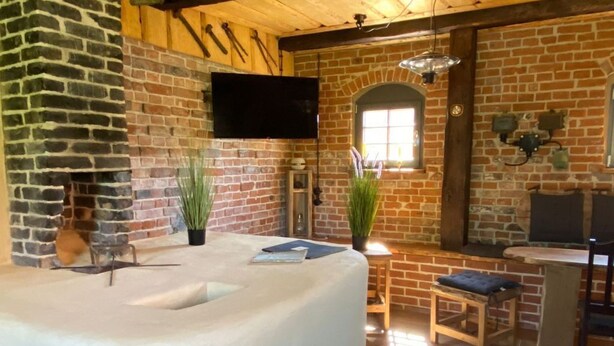 A spa area with a large, curved hot tub, a brick wall, and a wooden ceiling. - Alte Schmiede by Interhome (Boitzenburger Land)