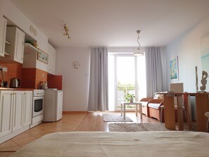 A modern kitchen with white cabinets, a stove, and a refrigerator. There is a dining area with a table and chairs, and a large window with curtains. - Helle Ferienwohnung in Kolberg mit Großem Balkon by Interhome (Kolobrzeg)