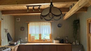 Eine rustikale Küche mit Holdekor, einem Gasherd, einer Spüle und einem Fenster mit Spitzenvorhang.