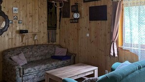 Ein gemütliches Blockhauss-Interieur mit Holzbalkendecke, einer Couch, einem Tisch und einem Fenster mit Vorhängen.