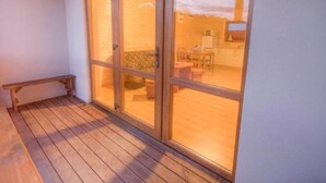 A wooden deck with a bench, a sliding glass door leading to a room with a kitchen and dining area. - "Cottage6" in einem eingezäunten Gebiet by Interhome (Mielno)