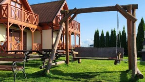 A wooden structure with a swing, a bench, and a building in the background. - "Cottage6" in einem eingezäunten Gebiet by Interhome (Mielno)