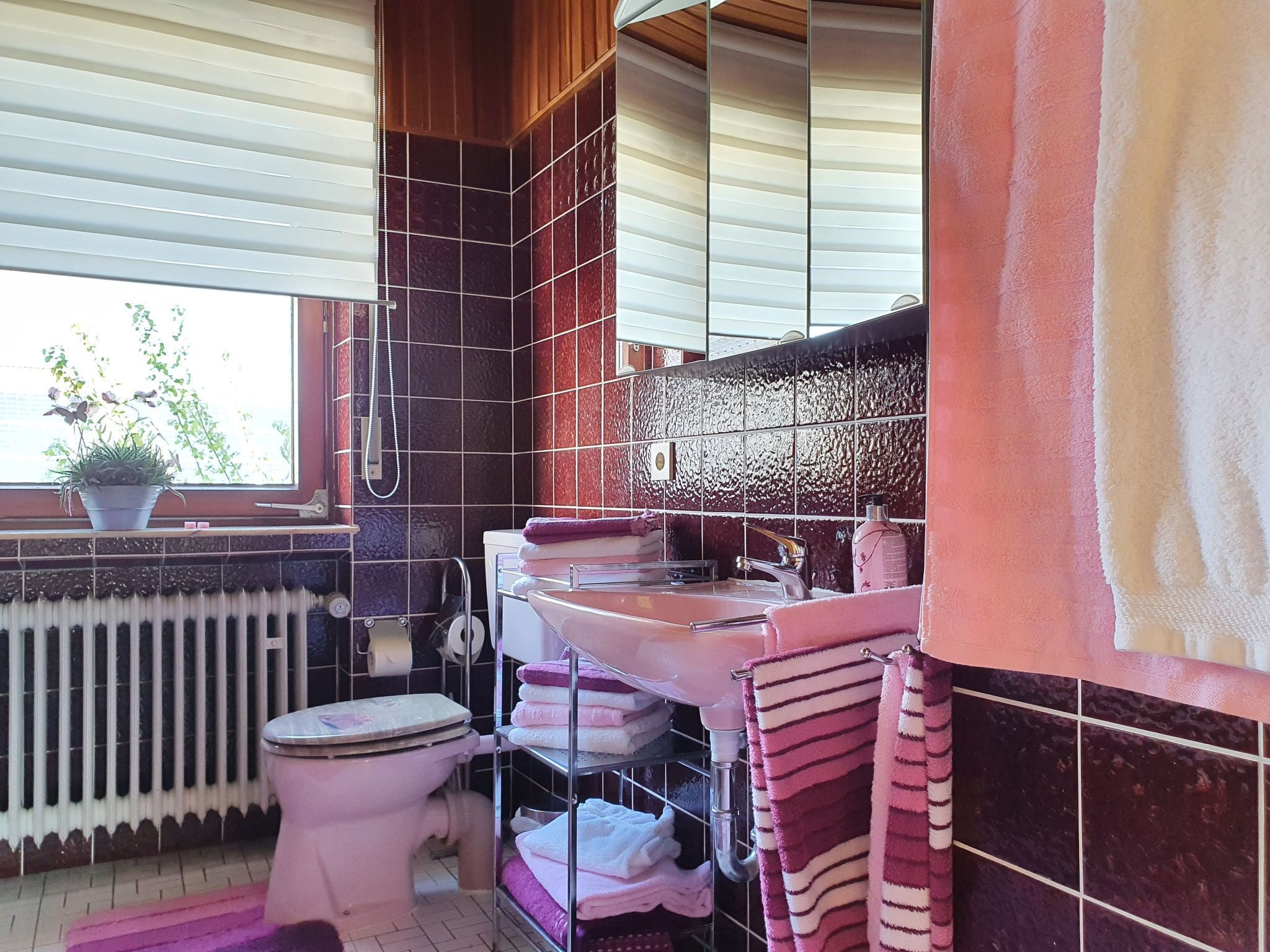 A bathroom with a toilet, sink, and shower. There is a window with a view of greenery outside.
