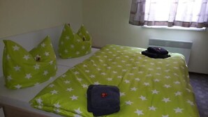 Ein Zimmer mit einem Einzelbett, einer grünen Bettdecke mit weißen Sternen, zwei Kissen und einer gefalteten Jackette auf dem Bett.