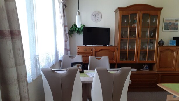 Ein Essbereich mit Tisch und Stühlen, einem Fernseher, einem Schrank und einer Wanduhr.