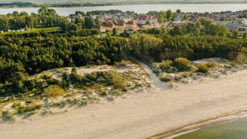 Vue aérienne d’une zone côtière comprenant une plage de sable, une forêt dense et une ville avec des maisons.
