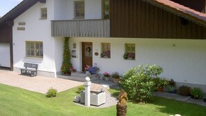 A two-story building with a sloped roof, a front porch, and a small garden area with potted plants and a bench. - Haus Annemarie by Interhome (Philippsreut)
