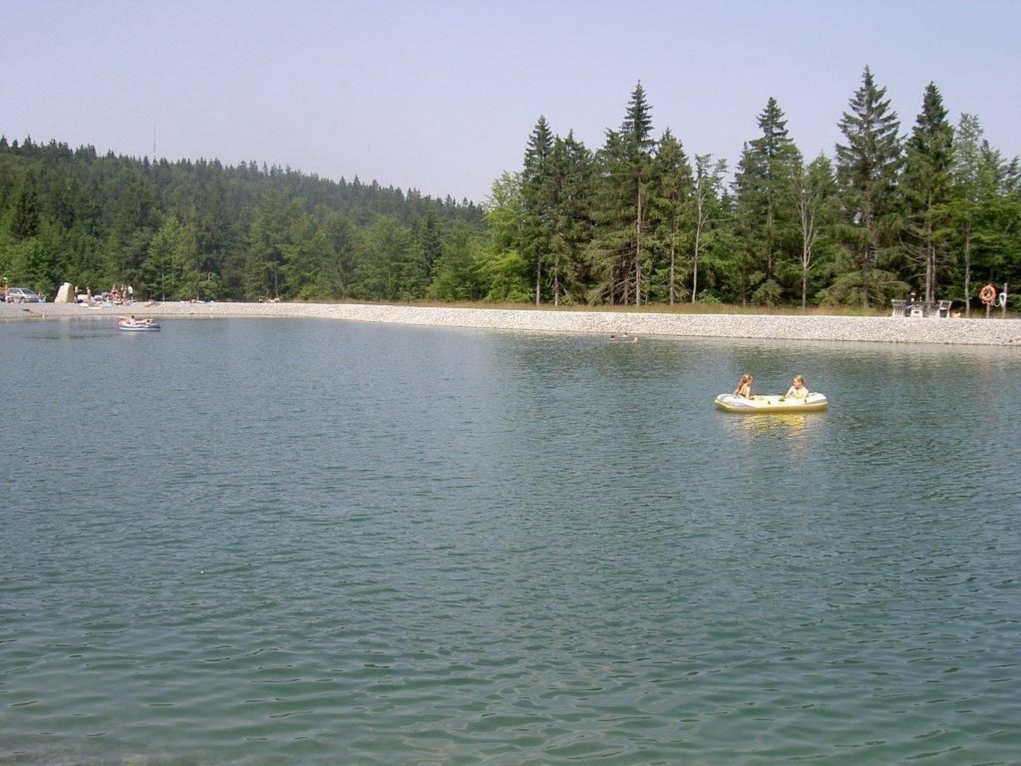 A calm lake with a small boat and a person in a raft.