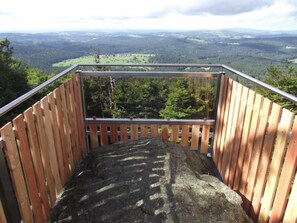 Eine Holztreppe führt zu einer Aussichtsplattform mit Metallgeländer, überblickt ein bewaldetes Tal.