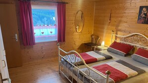 Een houten kamer met een bed, een stoel, een tafeltje en een raam met gordijnen.
