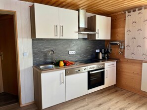 A compact kitchen with white cabinets, a stainless steel sink, a stove, and a microwave. - zur Linde by Interhome (Philippsreut)