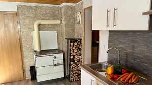 Een compacte keuken met een houtkachel, een spoelbak met groenten en een stenen muur.