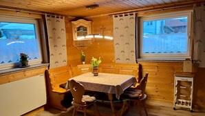 Een gezellig houten blokhut met een eethoek, compleet met tafel en stoelen, een kitchenette en een raam met gordijnen.
