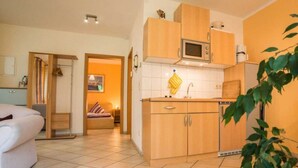 A compact kitchen with wooden cabinets, a microwave, and a sink. There is a bed with a striped pillow in the adjacent room. - mit Garten in ruhiger Lage by Interhome (Bansin)