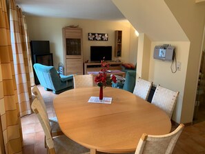 A dining area with a round table, chairs, a vase with flowers, a television, and a cabinet. - am Wasser mit Terrasse und Kaminofen by Interhome (Rechlin)