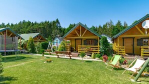 A row of wooden cabins with a grassy yard, a trampoline, and outdoor seating. - Haus in Gmina Postomino mit Garten und Terrasse by Interhome (Rusinowo)