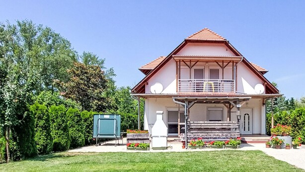 Ein zweistöckiges Haus mit Balkon, einer kleinen Veranda und einem Garten.