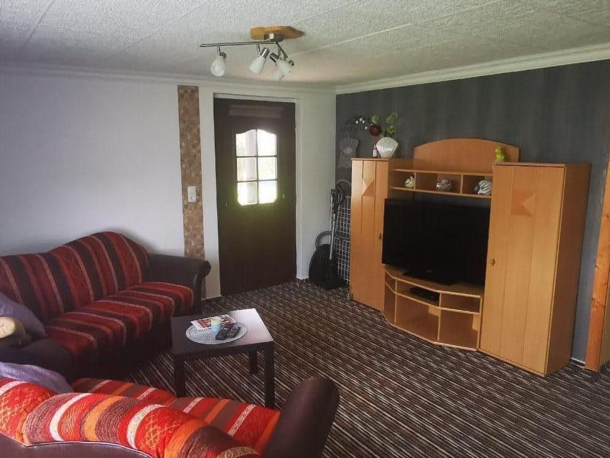 Un salon comprenant un canapé, une table basse, un téléviseur posé sur un meuble en bois et une porte avec une fenêtre.