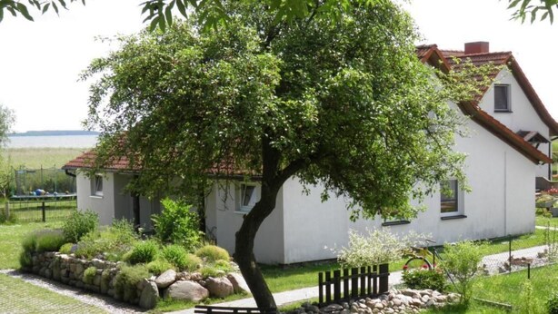 A white house with a red roof, surrounded by a well-maintained garden with a bench and a tree. - Appartement in Lütow mit Grill by Interhome (Krummin)