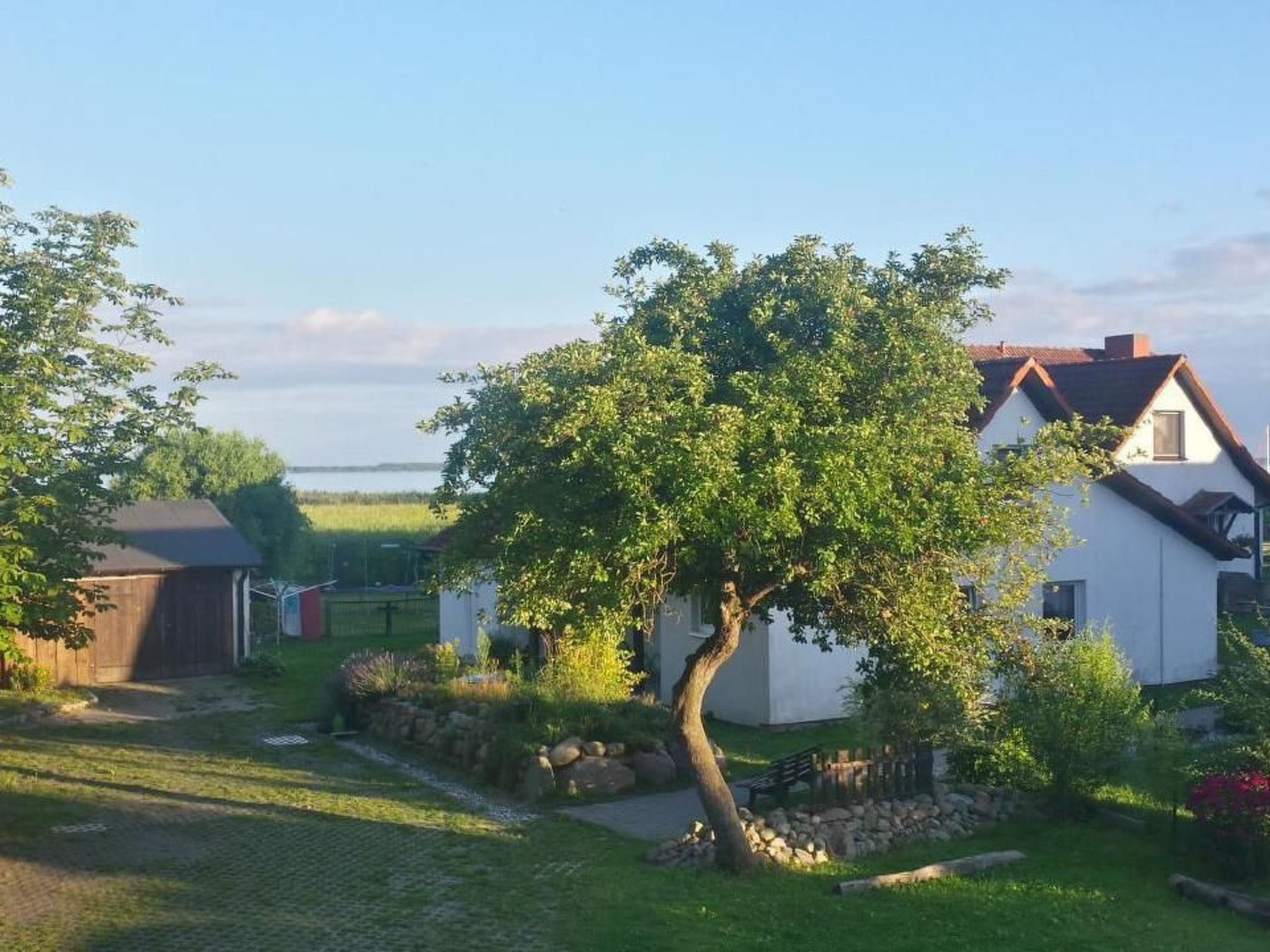 Ein weißes Haus mit geneigtem Dach, umgeben von einem gepflegten Garten mit einem großen Baum im Vordergrund.