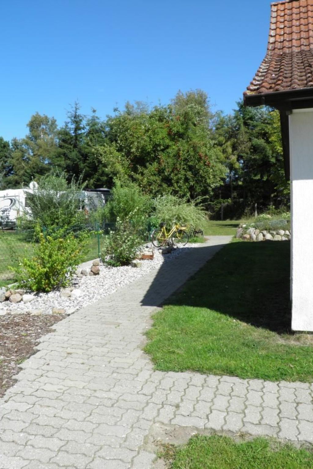 Un chemin pavé mène à un bâtiment dont le toit est recouvert de tuiles, entouré de verdure et où est garé un vélo.