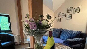 Ein Wohnzimmer mit einem Holztisch, einem Blumenstrauß, einer Weinflasche und einem Streifenmuster-Teppich.