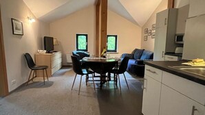 Ein gemütliches, helles Zimmer mit Esstisch, Stühlen, einer Sitzecke und einer Küchenzeile mit Schränken und einer Arbeitsplatte.
