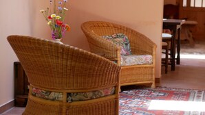 Zwei Korbstühle mit blumigen Kissen in einem Raum mit einem gemusterten Teppich und einer Blumenvase an der Wand.