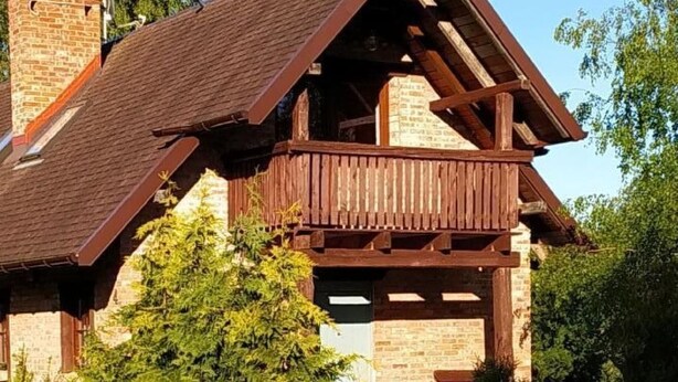 Una cabaña de madera con techo inclinado, balcón y base de piedra.