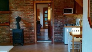 Un interior rústico con pared de ladrillo, un estufa de leña, una zona de comedor con mesa y sillas, y una cocina con microondas.