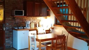 Una cocina con una escalera de madera, una mesa de comedor con sillas y un refrigerador.