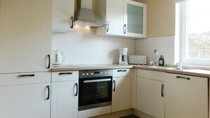 Una cocina moderna con armarios blancos, horno empotrado, cafetera y ventana que proporciona luz natural.