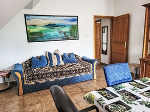 Un salon avec un canapé, une table recouverte d’une nappe à motifs et un tableau accroché au mur.