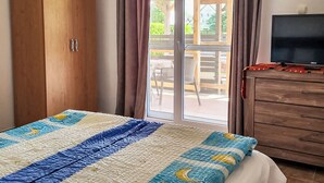 Une chambre à coucher comprenant un lit, une armoire en bois, un téléviseur et une porte-fenêtre coulissante donnant sur une terrasse extérieure.