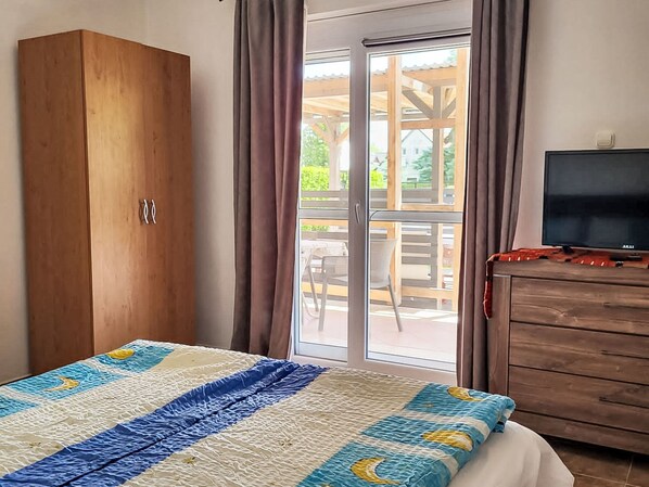 A bedroom with a bed, a wooden wardrobe, a television, and a sliding glass door leading to an outdoor patio. - Vacation home am See by Interhome (Balatonmariafurdo)