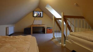 A small, sloped-roofed room with a wooden desk, two beds, a TV mounted on the wall, and a staircase leading to an upper level. - Maisonette  Seebrise mit Seeblick am Strand by Interhome (Flessenow)