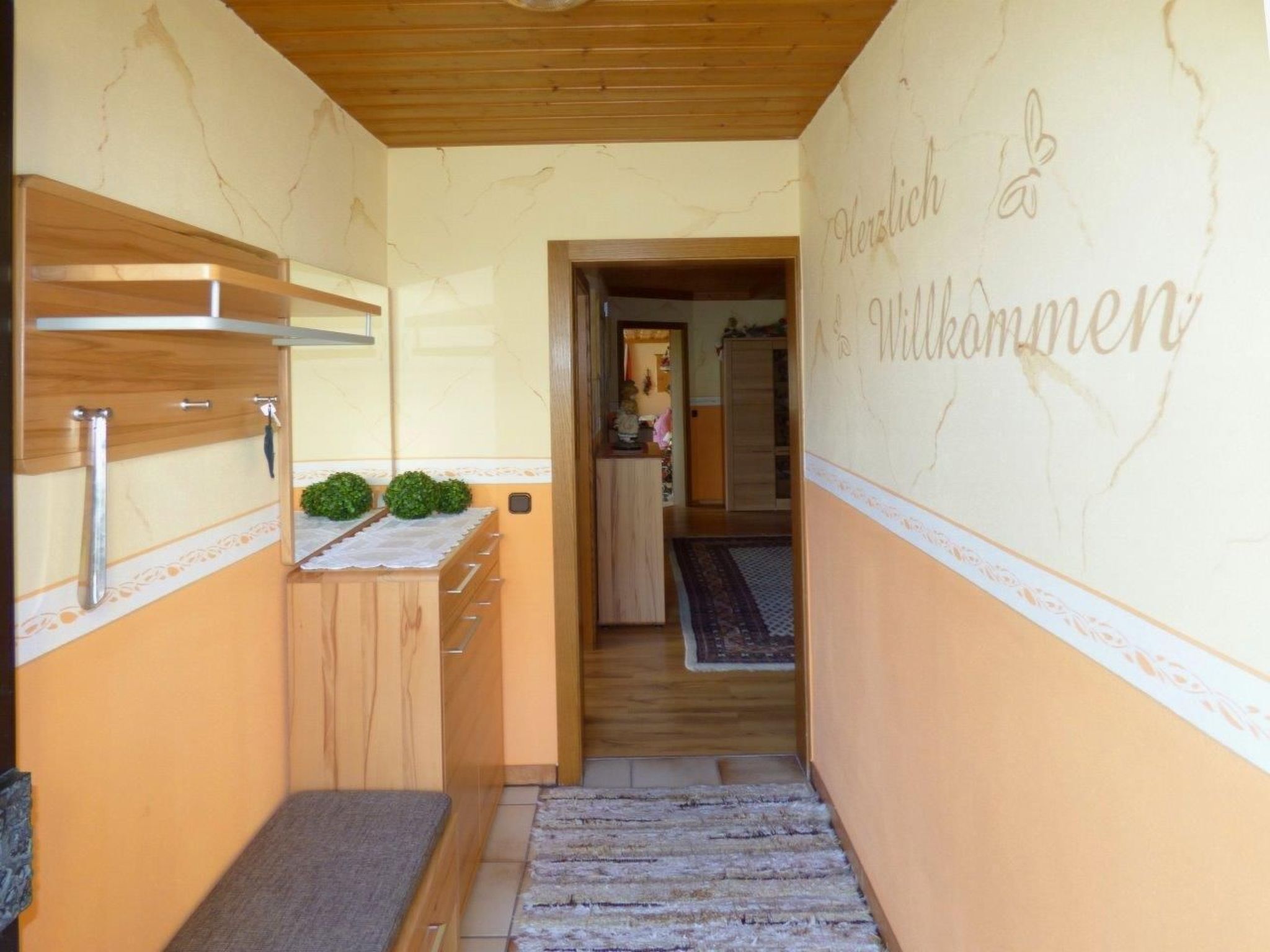 A hallway with a wooden ceiling, a reception desk, and a wall with the text "Herzlich Willkommen".