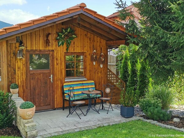 Una cabaña de madera con porche, un banco a rayas y una pequeña mesa.