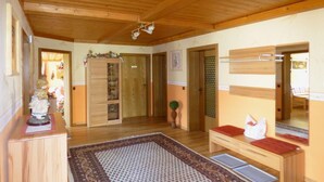 Ein Zimmer mit Holzboden, einem gemusterten Teppich, einer Bank mit rotem Kissen und einem Holzkasten mit einem dekorativen Gegenstand darauf.