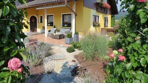 Ein gelbes Haus mit überdachter Terrasse, Sitzgelegenheiten im Freien und einem Garten mit Blumen und Pflanzen.
