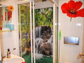Een badkamer met een glazen douchecabine, een wastafel, een spiegel en een rood bloemdecoratie.
