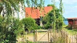 Una propiedad rural con un portón de madera, abundante vegetación y un edificio de techo rojo.