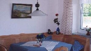 Un coin repas avec un banc et une table en bois, un luminaire suspendu, un tableau au mur et une fenêtre avec des rideaux.