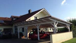 Une maison avec un garage fermé, une voiture rouge garée à l’intérieur, et un ciel bleu dégagé.