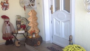 Un hall d’entrée avec une porte blanche, un lustre, une pancarte de bienvenue, une petite table sur laquelle est posé un ours en peluche et une plante en pot.