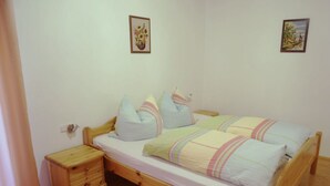 Habitación individual con una cama de madera, una mesita de noche pequeña y dos cuadros colgados en la pared.