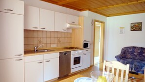 Cocina compacta con armarios blancos, encimera de madera, lavabo, microondas y lavavajillas.  Comedor con mesa, sillas y un jarrón con una flor amarilla.